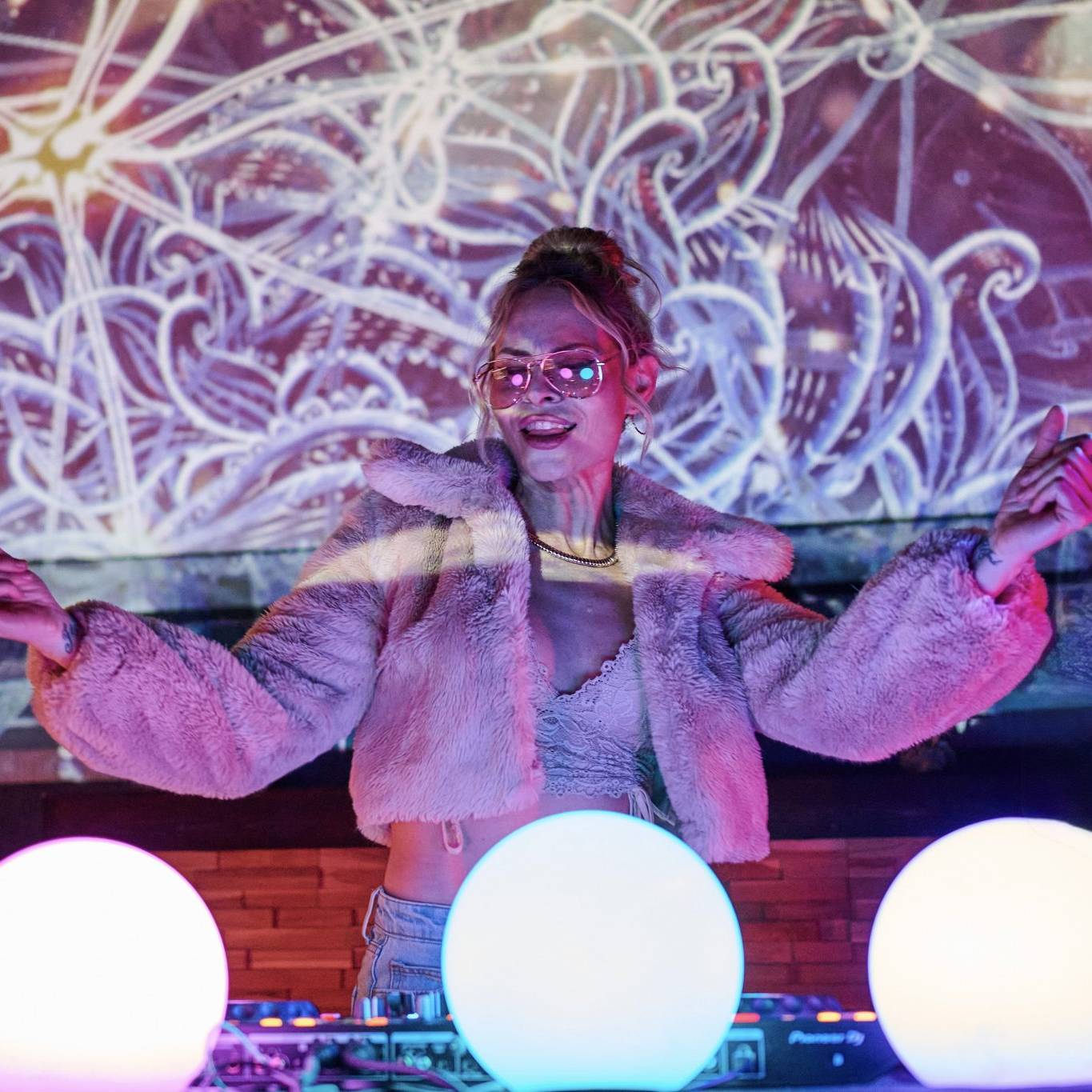 Kat Walsh performing a Kat’s Meow DJ set with purple and pink psychedelic visuals projected behind her.