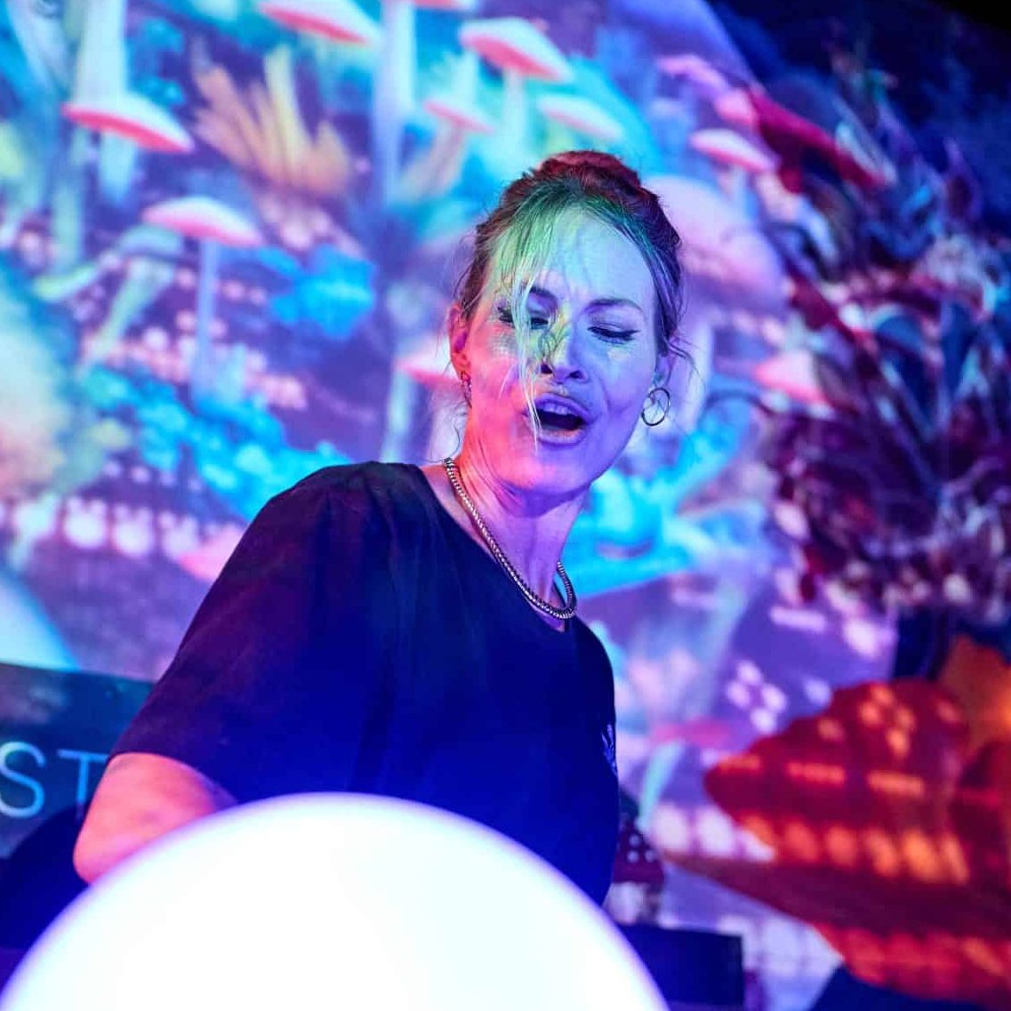 Kat Walsh DJing as her alias Kat's Meow. Psychedelic colorful background