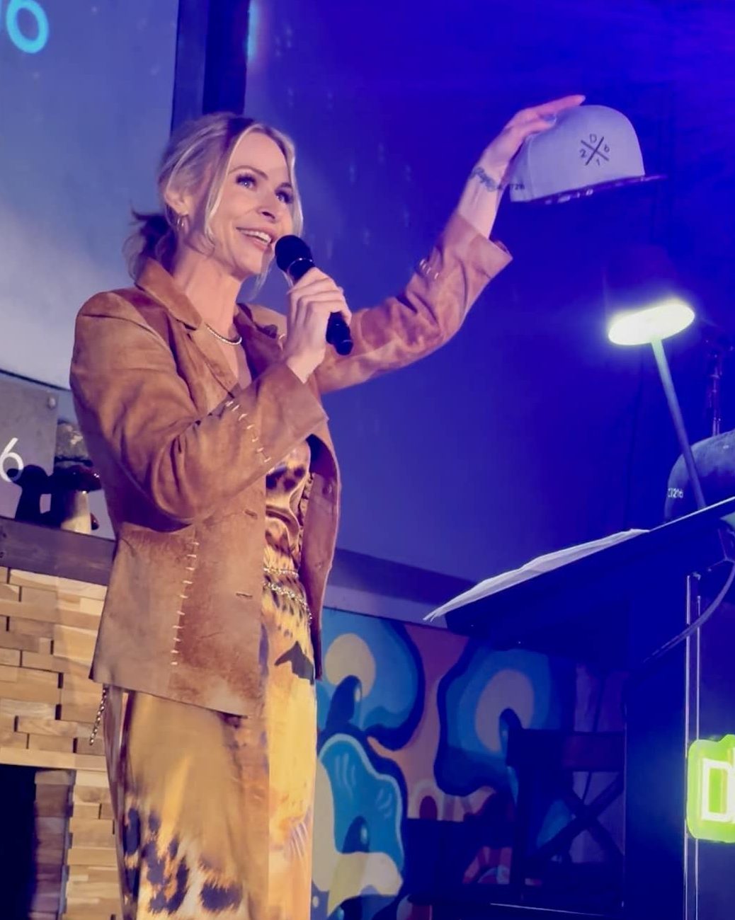 Kat Walsh speaking on stage as a psychedelic show host and event moderator.